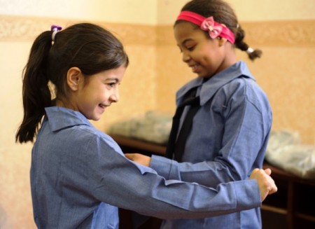 Mona, 8, and her new friend, Maysam, 9, are overjoyed with the new uniforms that will allow them to attend a Jordanian public school this fall.  IOCC is providing school uniforms to more than 30,000 Syrian refugee children living in Jordan to support the continuation of their education. PHOTO: Anas Bino/IOCC