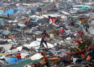 A man stands atop debris as residents salvage belongings from the ruins of their houses after Typhoon Haiyan battered Tacloban city in central Philippines November 10, 2013. The destructive force of the storm has left more than 920,000 people homeless and in desperate need of food, water, and medical attention. IOCC is working with relief partners on the ground to provide aid to residents of hard hit Tacloban and surrounding communities. CREDIT: REUTERS/Erik De Castro – Courtesy of trust.org