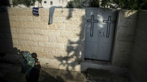 A Palestinian woman carrying an infant is pictured at the entrance of Gaza City’s Greek Orthodox church compound on July 23, 2014 where around 600 people, mostly women and children, are sheltering (photo credit: AFP/Marco Longari)
